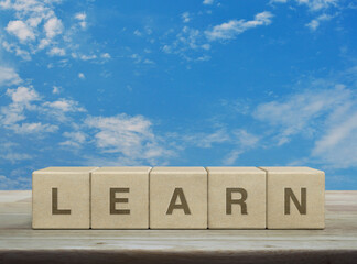 Learn letter on wood block cubes on wooden table over blue sky with white clouds, Business, education and learning concept