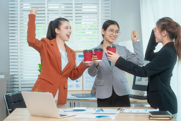 Three Asian women in formal suits collaborate at a desk, discussing documents in a modern office....