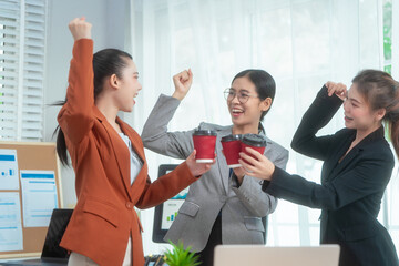 Three Asian women in formal suits collaborate at a desk, discussing documents in a modern office....