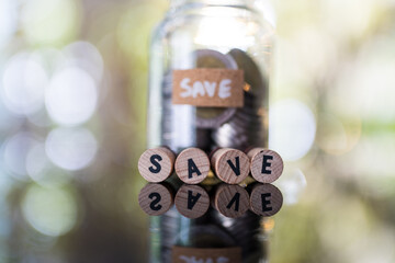 Wooden blocks displaying SAVE in font of glass jar bank fill with coin, symbolizing financial save...