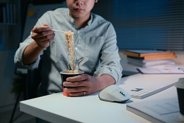 Young businessman eating instant noodles while working late at the office