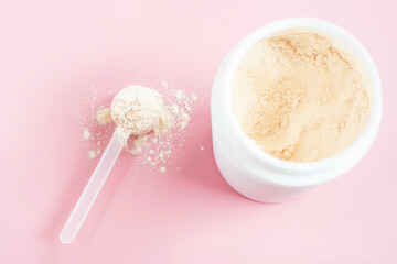 Protein powder in scoop against plastic jar on pink background, top view.