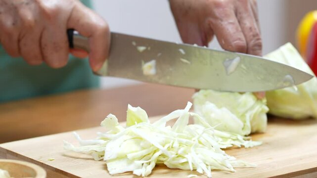 Closeup of male hands slicing Cabbage on a wooden board in the kitchen, preparing to cook.