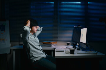 Exhausted male employee working overtime alone at night in dark office