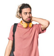 Young student with backpack and headphones touching back of head, thinking and making a choice.