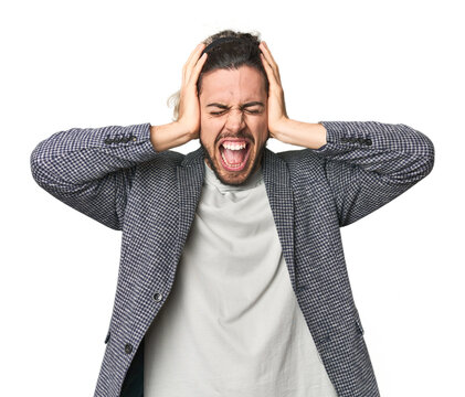 Young businessman in casual blazer covering ears with hands trying not to hear too loud sound.