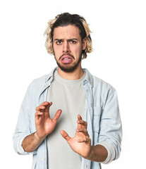 Young Caucasian man in studio setting rejecting someone showing a gesture of disgust.