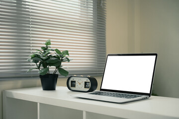 Office desk featuring laptop with blank screen, a potted plant, and a vintage flip clock