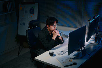 Focused businessman working late night on desktop computer in dark office