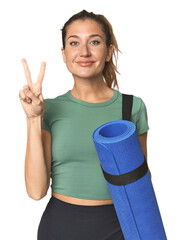 Blonde athlete holding a yoga mat showing number two with fingers.