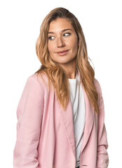 Young blonde in stylish pink suit looks aside smiling, cheerful and pleasant.