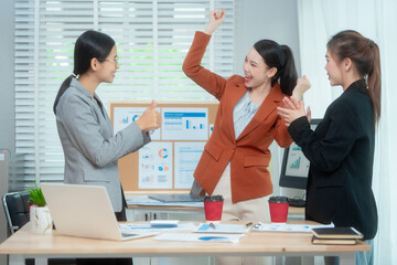 Three Asian women in formal suits collaborate at a desk, discussing documents in a modern office. teamwork, strategy planning, creative problem-solving in professional business environment.