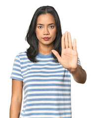 Young Latina posing in studio standing with outstretched hand showing stop sign, preventing you.