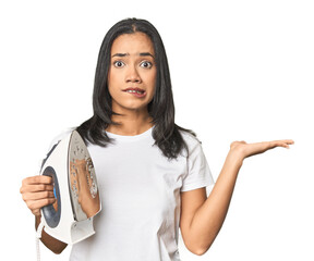 Latina with iron, studio setup confused and doubtful shrugging shoulders to hold a copy space.