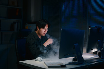 Young businessman working late at night while vaping in dark office