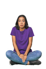 Latina sitting on floor in studio shrugs shoulders and open eyes confused.