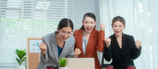 Three Asian women in formal suits collaborate at a desk, discussing documents in a modern office....