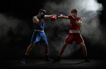 Boxers in blue and red engage in an intense fight amidst smoke on a dark background. Concept of...