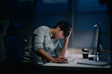 Exhausted male employee working overtime alone at night in dark office