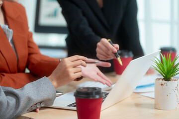 Three Asian women in formal suits collaborate at a desk, discussing documents in a modern office....