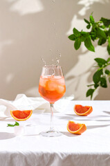 A dynamic splash of an orange Aperol Spritz, with ice cubes and blood orange slices, captured as they fall into the glass on a white table.