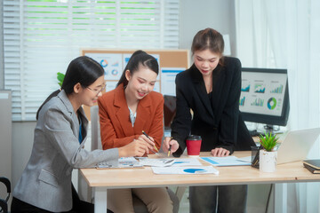 Fototapeta premium Three Asian women in formal suits collaborate at a desk, discussing documents in a modern office. teamwork, strategy planning, creative problem-solving in professional business environment.