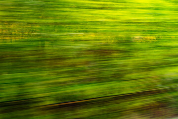 Dynamic motion blur view from high-speed train window: Green landscape, trees & fields rush past at high speed