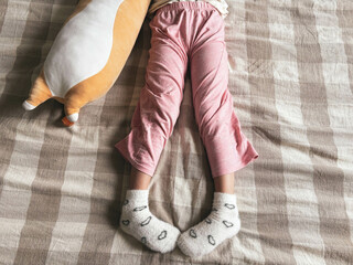 Legs of a girl about 5 years old and plush cat toys on the bed. The child plays on the bed.