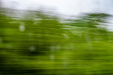Dynamic motion blur view from high-speed train window: Green landscape, trees & fields rush past at...