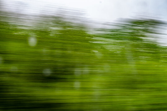 Dynamic motion blur view from high-speed train window: Green landscape, trees & fields rush past at high speed