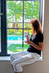 young woman is looking through the window with a cup of coffee