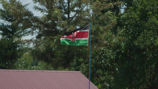 National flag flutters in wind above roof of house in settlement on Mount Elgon against backdrop of green trees