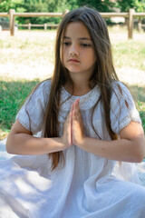 Young girl lying on a blanket in a park performing a yoga pose She is wearing a white lace top and...