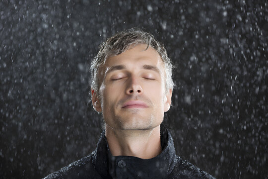 Man standing in the rain with eyes closed, peaceful expression. Symbol of emotional release, renewal, and freedom.