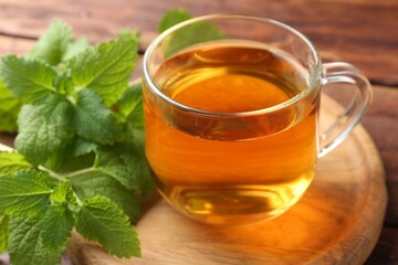 Aromatic lemon balm tea in glass cup and fresh leaves on table, closeup