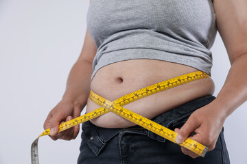 Overweight woman measuring her belly with tape on light background, closeup