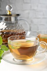 Aromatic lemon balm tea in glass cups, teapot and fresh leaves on white table, closeup
