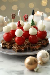Tasty canapes and Christmas decor on white marble table against background with blurred lights, closeup. Bokeh effect