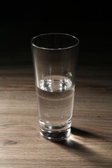 Fresh water in glass on wooden table against dark background