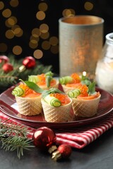 Tasty canapes and festive decor on black table against blurred lights, closeup. Bokeh effect