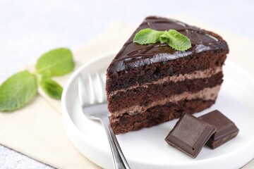 Piece of delicious cake, mint, chocolate and fork on light table, closeup