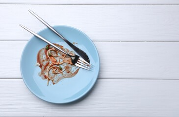 Dirty plate with spaghetti, peas, tomato sauce and cutlery on white wooden table, top view. Space...