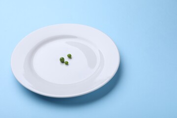 Plate with fresh green peas on light blue background, closeup. Space for text