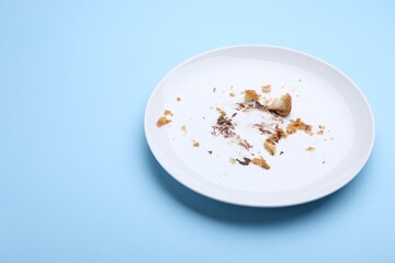 Dirty plate with crumbs and cream on light blue background, closeup. Space for text