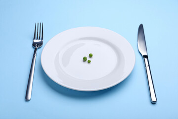 Plate with fresh green peas and cutlery on light blue background, closeup