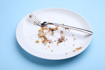 Dirty plate with crumbs, cream and fork on light blue background, closeup