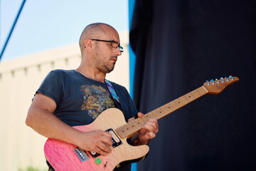 Rock band member performs on stage during outdoor festival in sunny weather