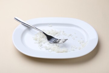 Dirty plate with rice and fork on beige background, closeup