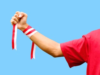 Hand with clenched fist wearing red and white ribbon on blue background during Indonesia's independence day celebration, copy space