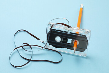 Rewinding audio cassette with pencil on light blue background
